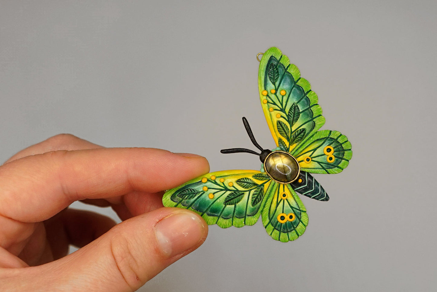 Hand holding a green and yellow butterfly-shaped object against a gray background