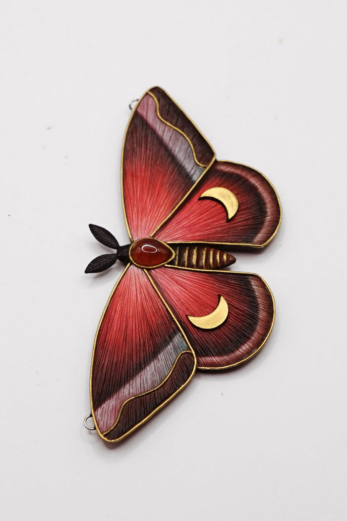 Red butterfly-shaped pendant with gold accents on a white background