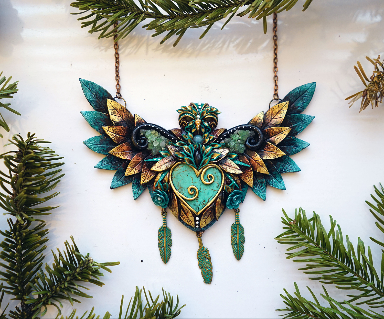 Decorative polymer clay necklace with green and gold elements on a white background with greenery.