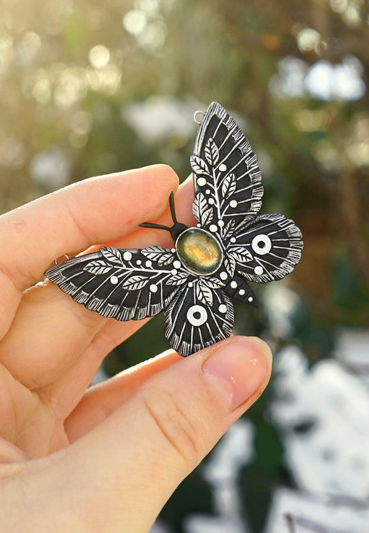 Hand holding a detailed moth-shaped object with a blurred natural background