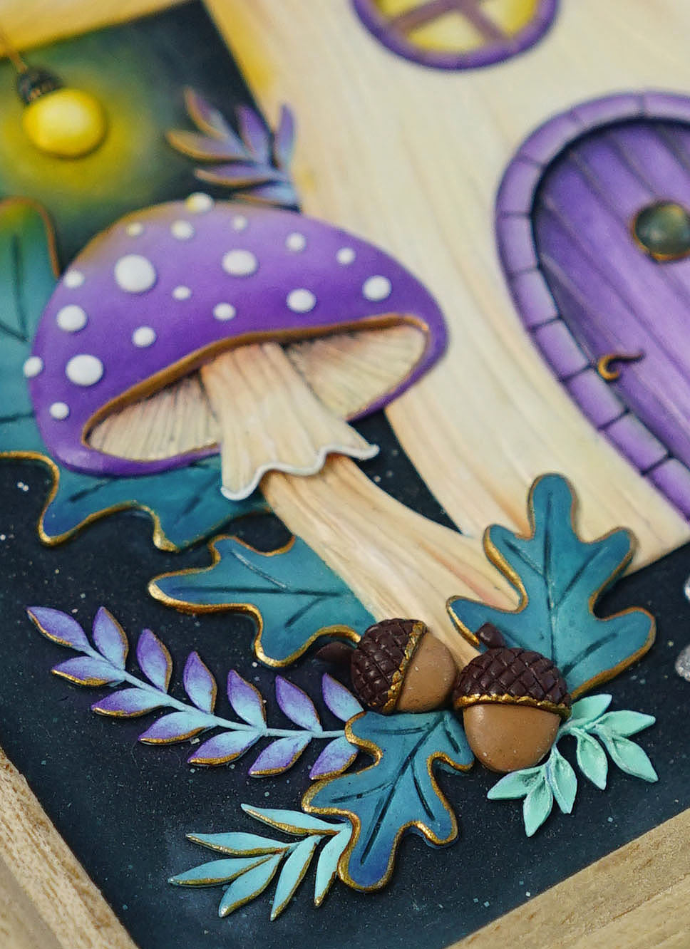 A close-up of a decorative fairy tale house panel with a large purple spotted mushroom, teal and green leaves, acorns, and a purple door on a light wood background.