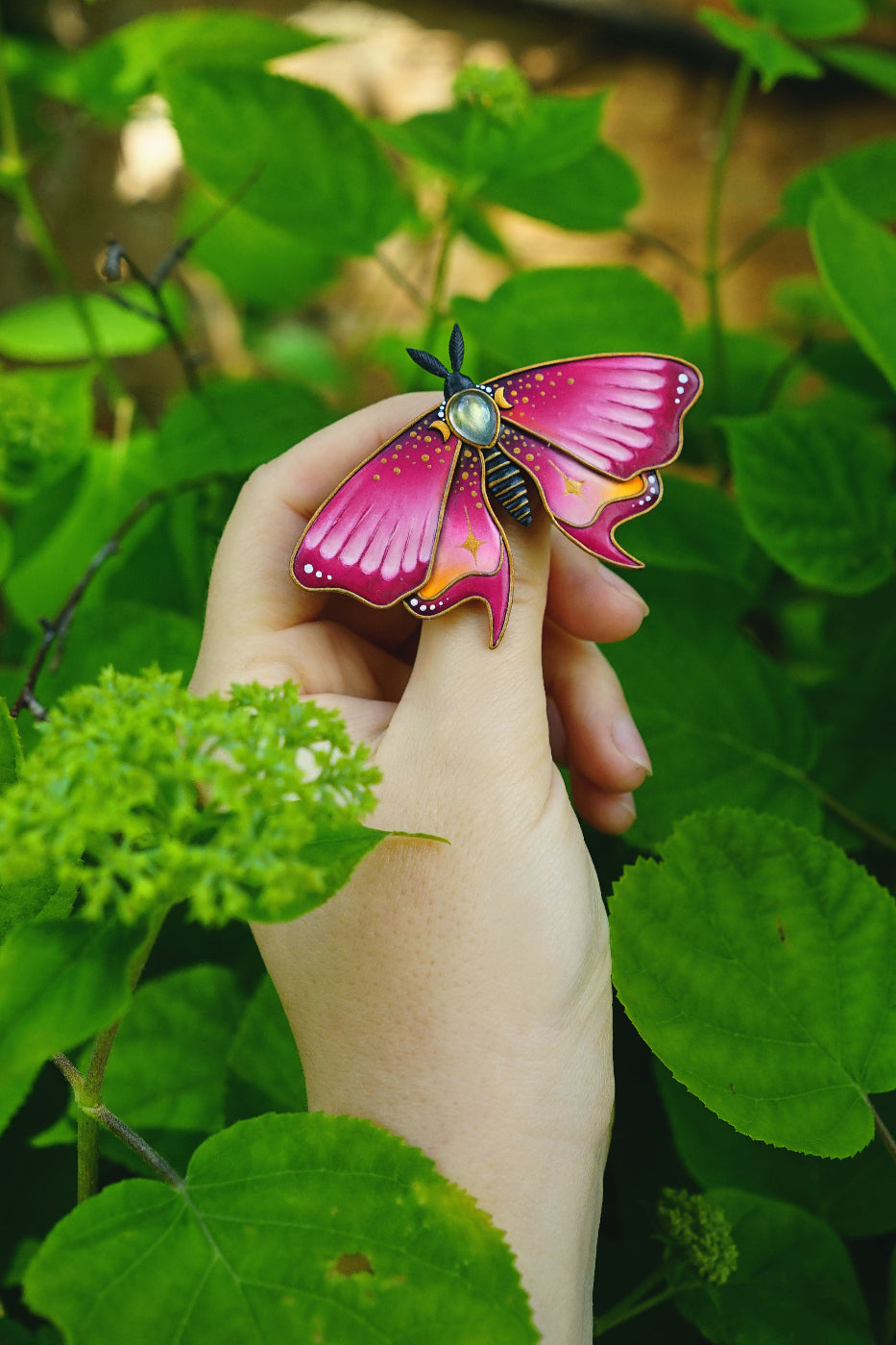 Hand holding a pink butterfly-shaped object against a green leafy background