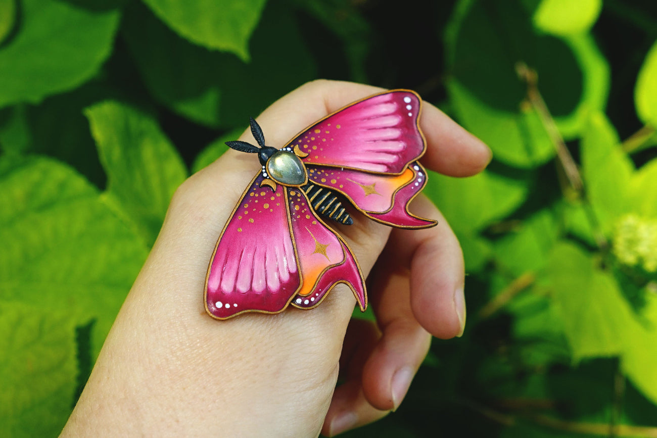 Hand holding a pink butterfly-shaped object against a green leafy background