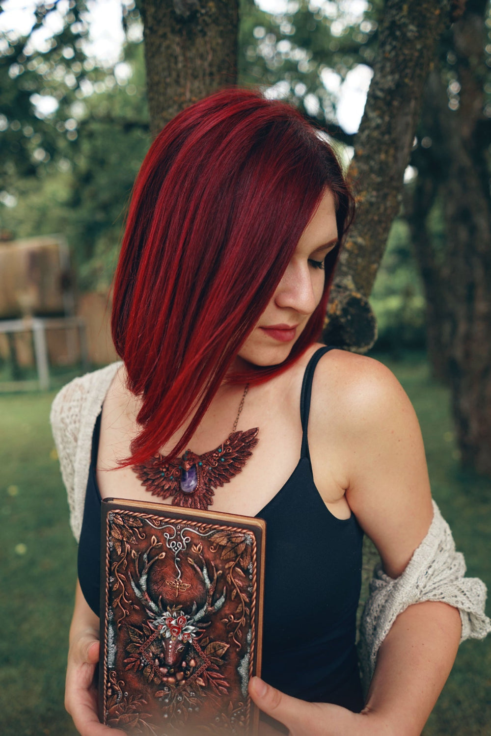 Woman with red hair holding a polymer clay journal in a forest setting