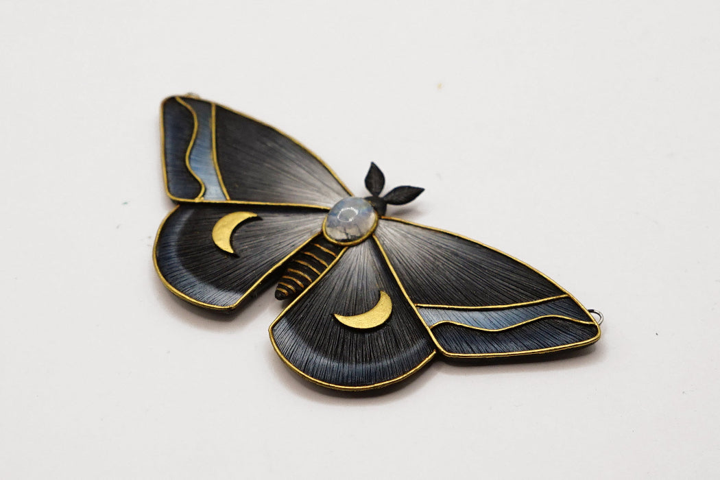 Decorative moth-shaped object with gold accents on a white background