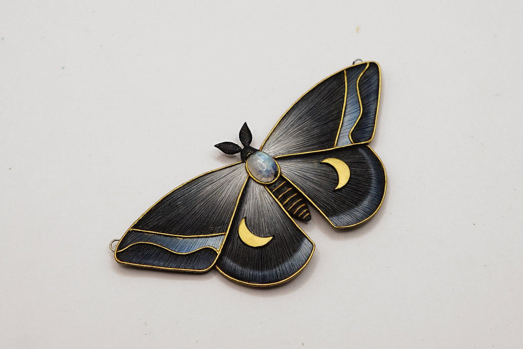 Moth-shaped brooch with gold accents on a white background