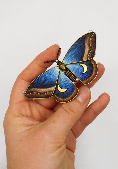Hand holding a blue and gold butterfly-shaped object against a white background