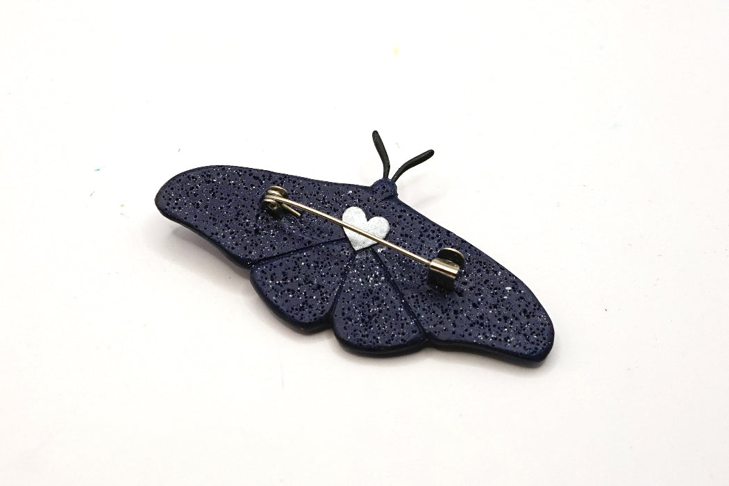 Black glittery butterfly-shaped brooch with a white heart on a white background