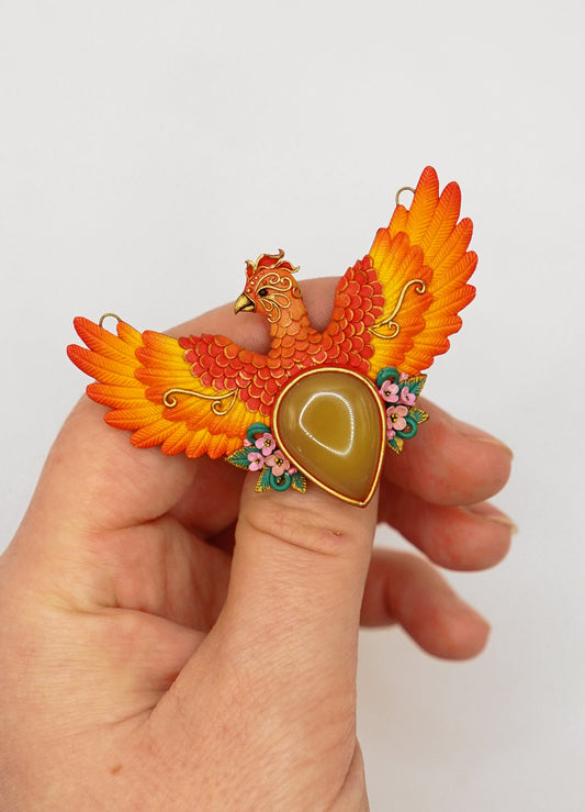 Hand holding a colorful phoenix-shaped object with a heart design on a white background