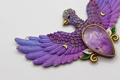 Purple and gold bird-shaped decorative item with a large purple stone on a white background