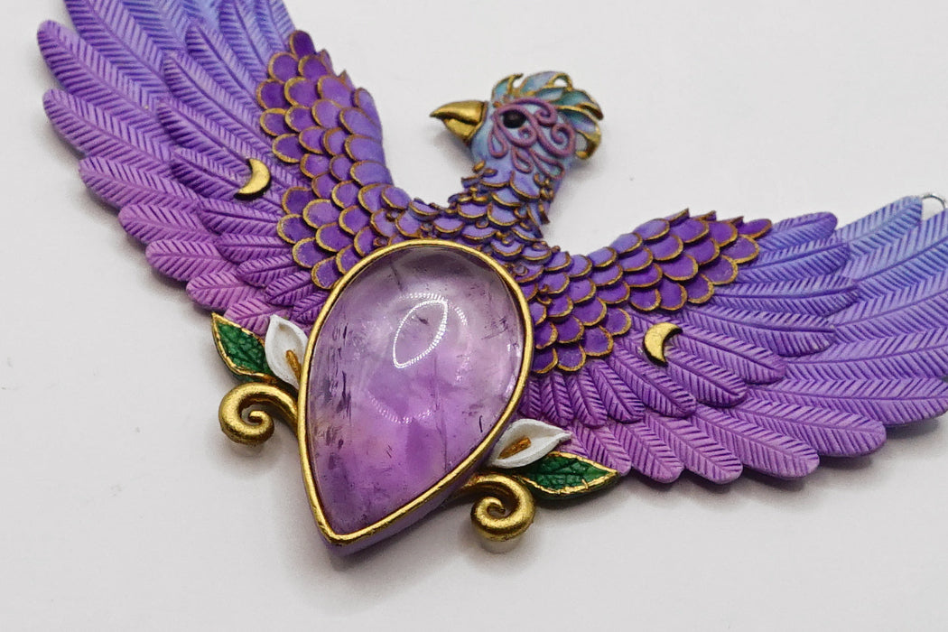 Purple feathered bird pendant with a large purple gemstone on a white background