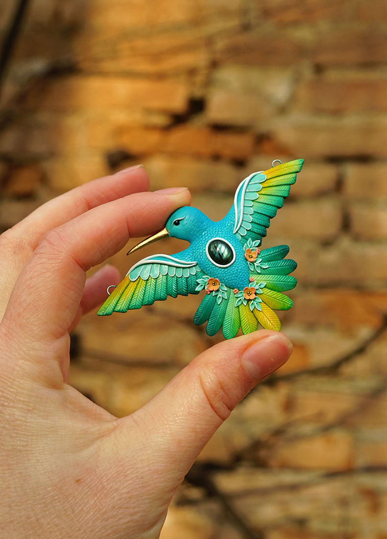 Hand holding a colorful hummingbird-shaped object against a brick wall background