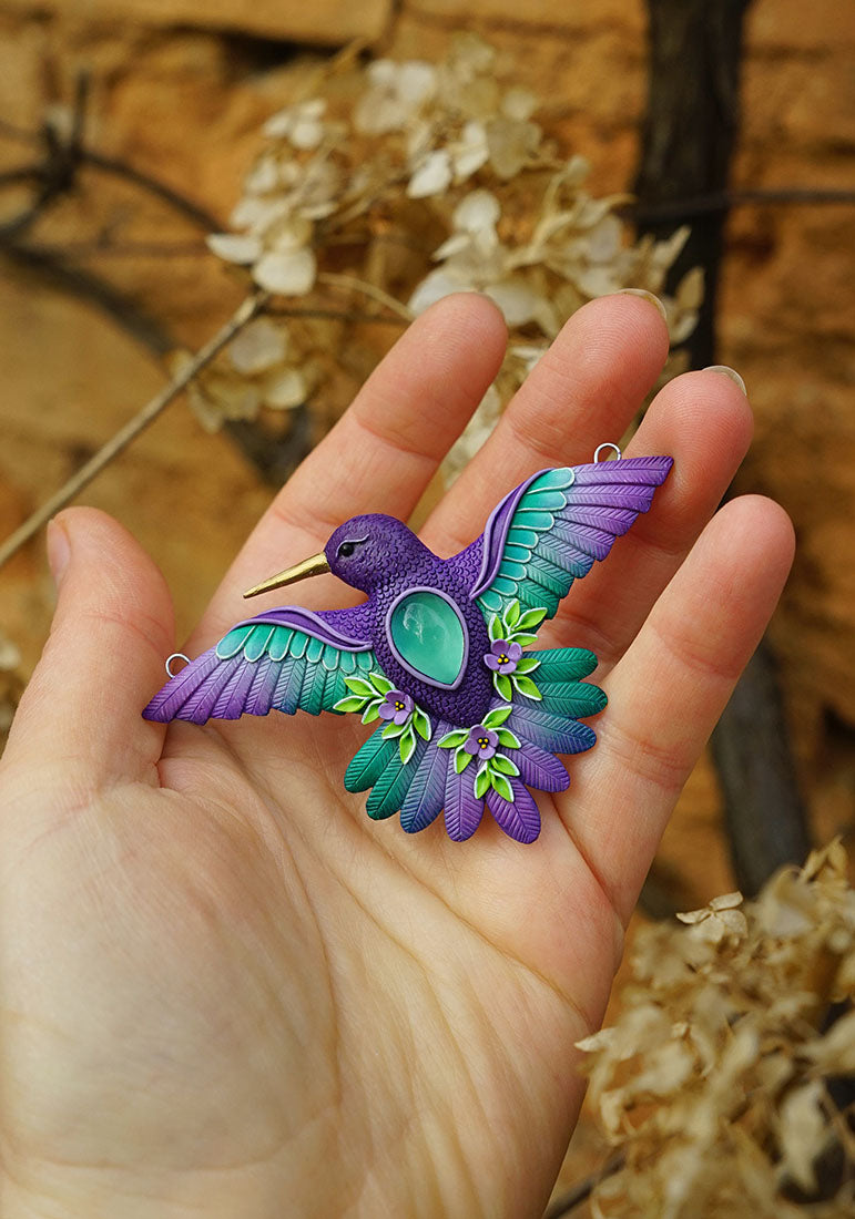 Hand holding a colorful hummingbird-shaped pendant against a natural background