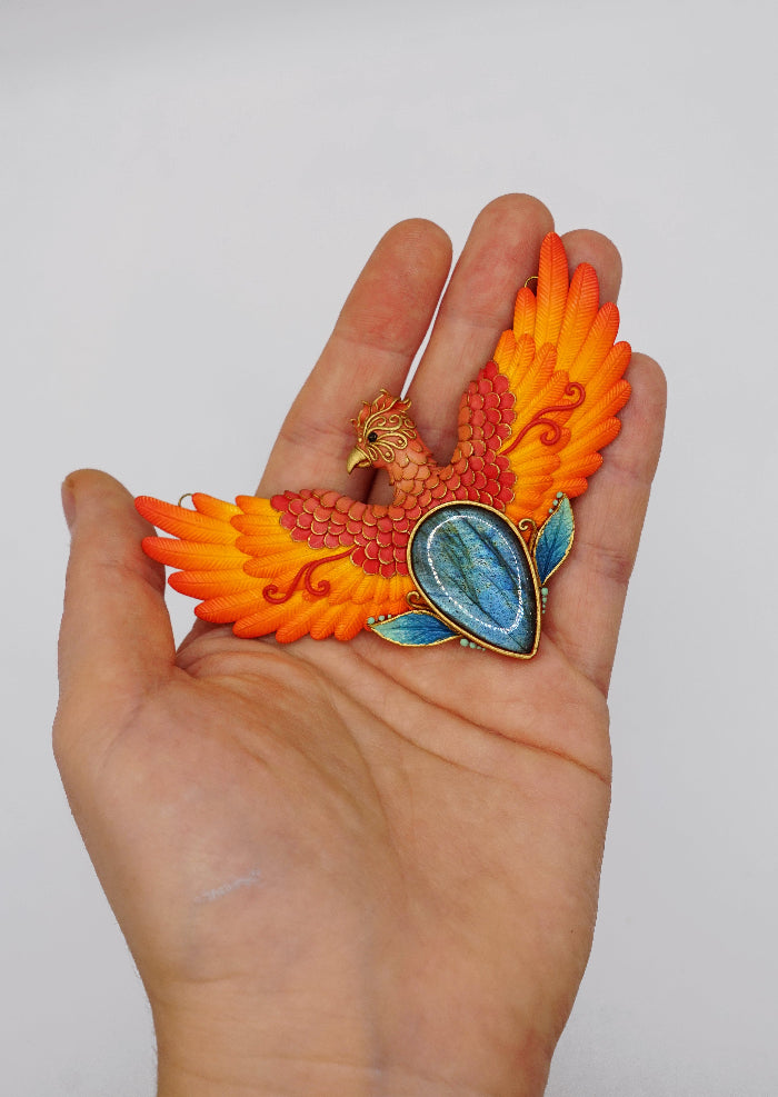 Colorful phoenix-shaped object held in a hand against a white background