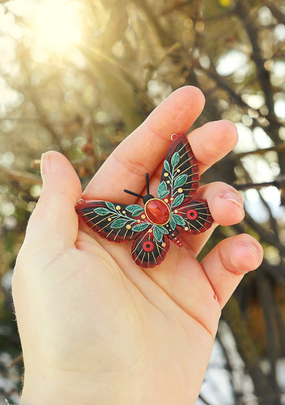 Hand holding a decorative butterfly pendant with a blurred natural background