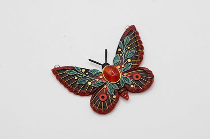 Decorative butterfly brooch with red and green details on a white background