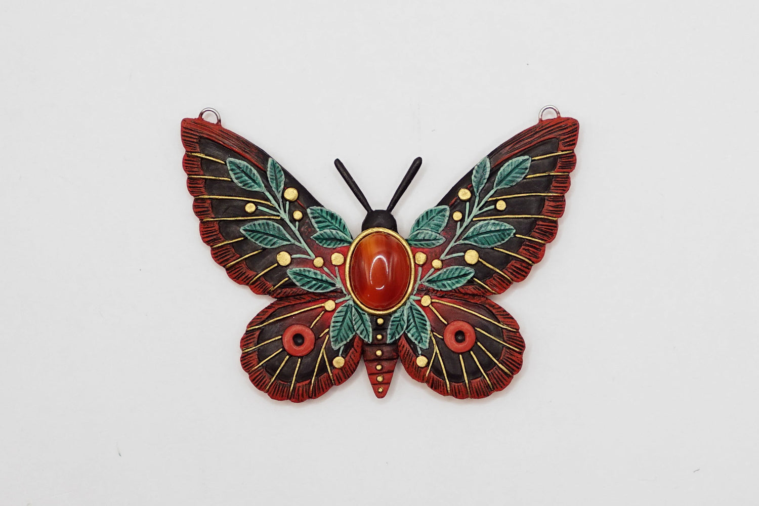 Decorative butterfly pendant with red center and green leaves on a white background