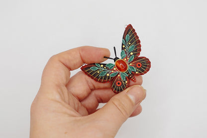 Hand holding a decorative butterfly pin against a plain background