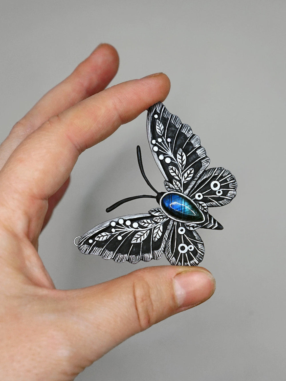 Hand holding a detailed black and white butterfly with blue accents against a gray background