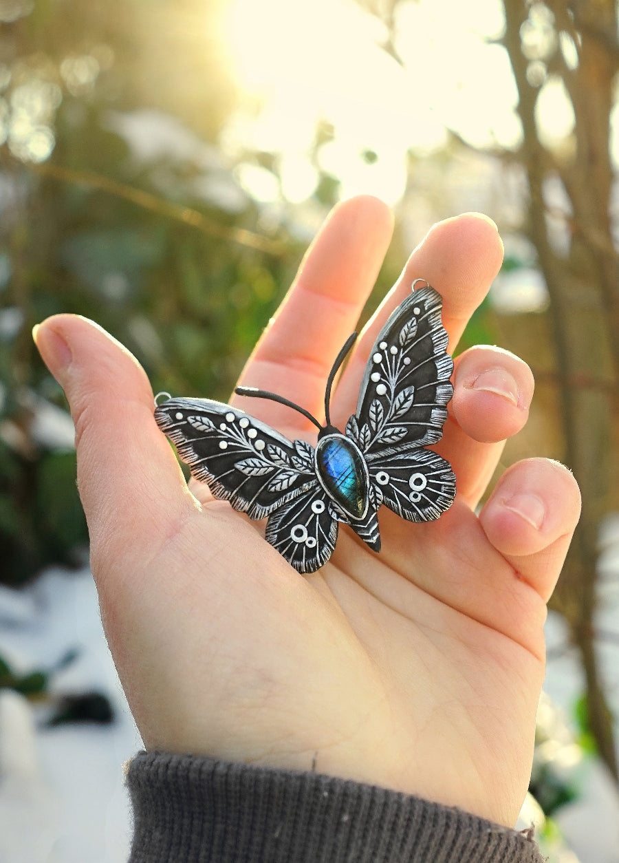 Butterfly-shaped pendant held in a hand with a blurred natural background