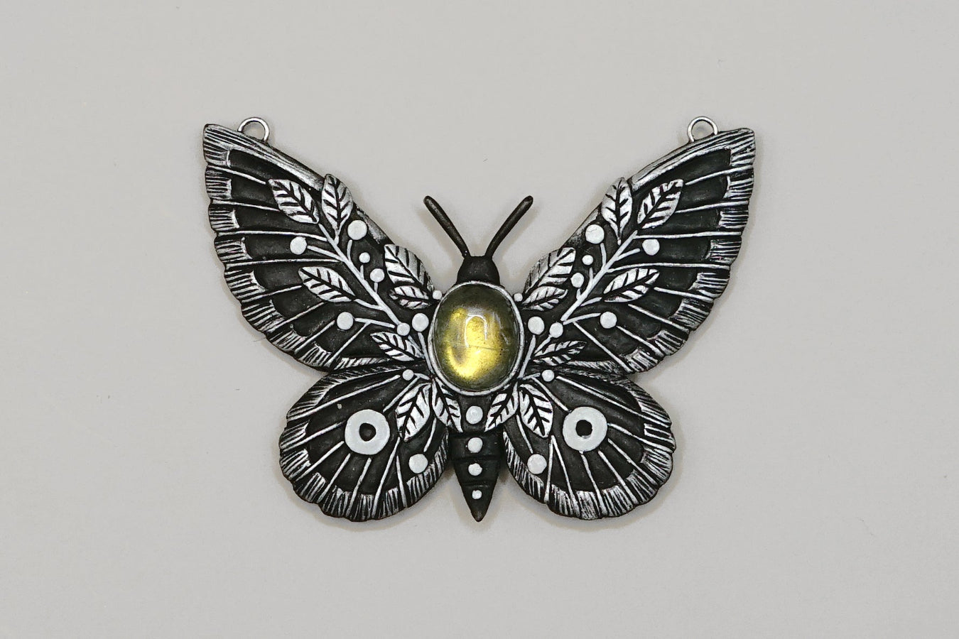 Butterfly-shaped pendant with a central yellow gem on a gray background