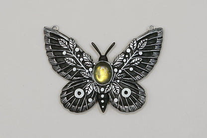 Butterfly-shaped pendant with a central yellow gem on a gray background