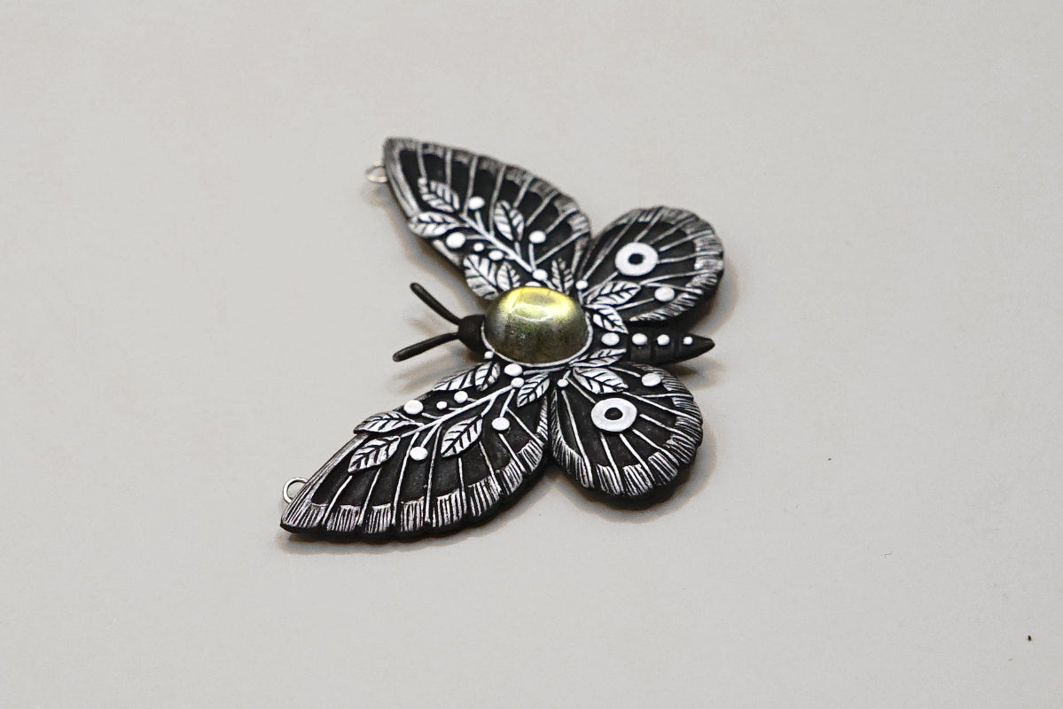 Butterfly-shaped pendant with intricate details on a light gray background