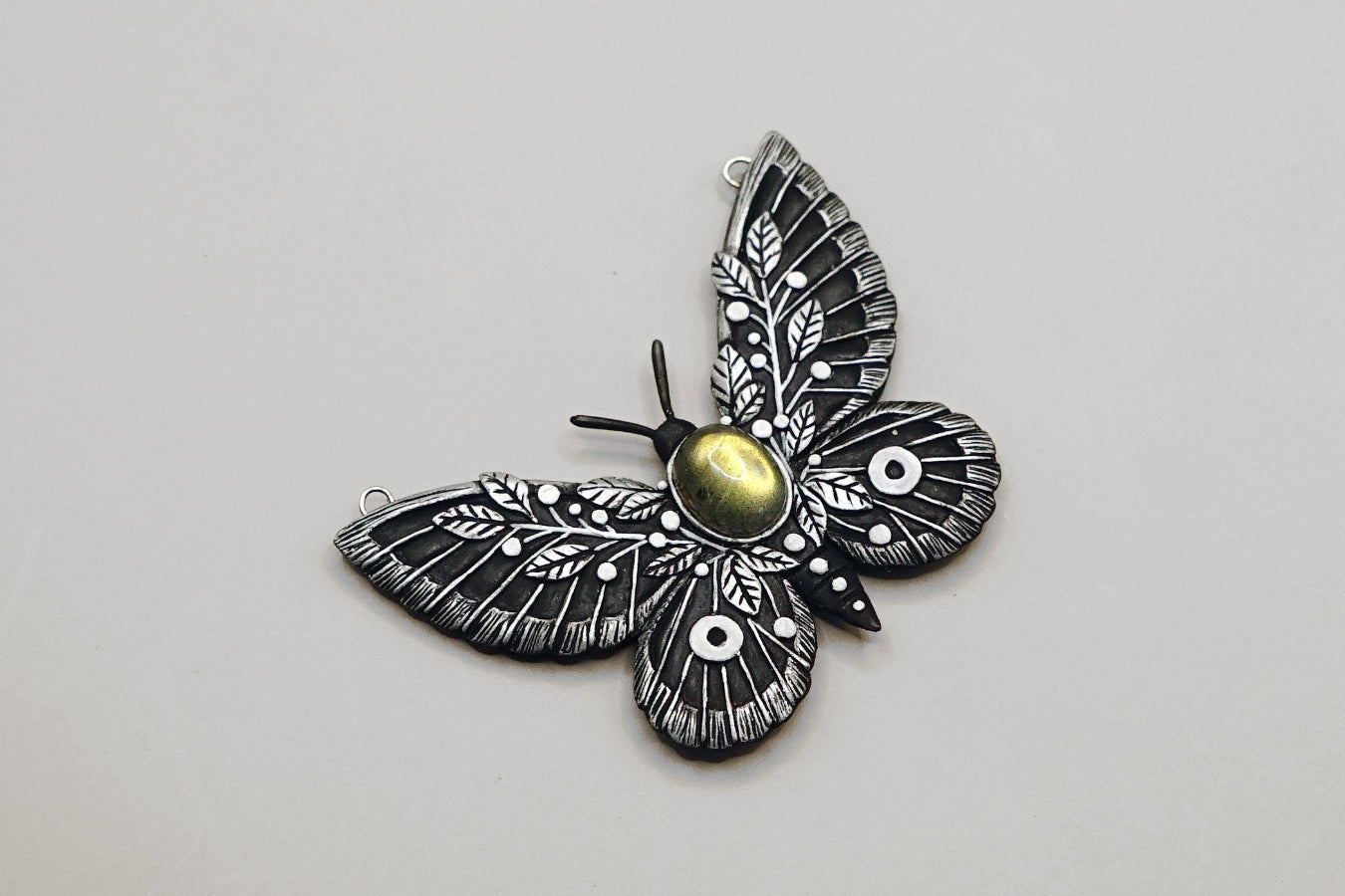 Butterfly-shaped pendant with intricate design on a light gray background
