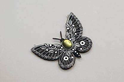 Butterfly-shaped pendant with intricate design on a light gray background
