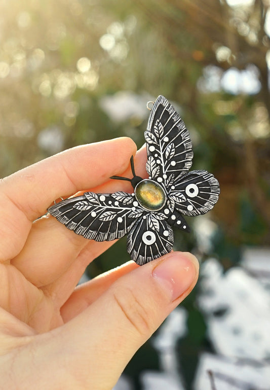 Hand holding a detailed moth-shaped object with a blurred natural background