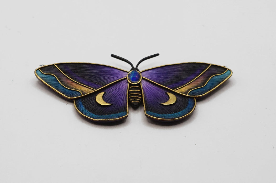 Butterfly-shaped brooch with purple and gold colors on a white background