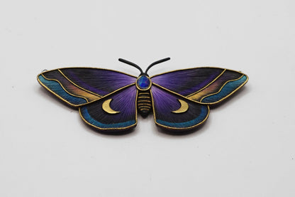 Butterfly-shaped brooch with purple and gold colors on a white background