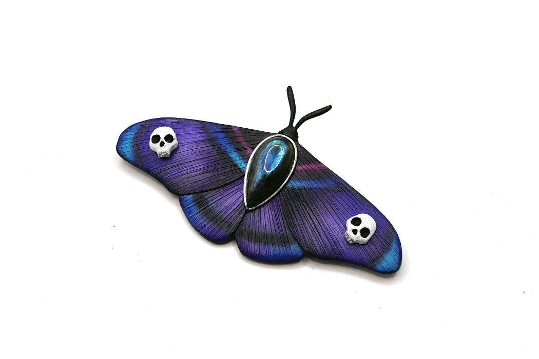 Purple butterfly-shaped brooch with skull designs on a white background